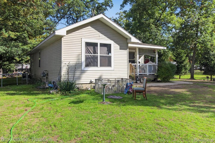 Vinyl-sided exterior featuring a gable roof, covered porch with a wooden railing, and mature trees on the surrounding…
