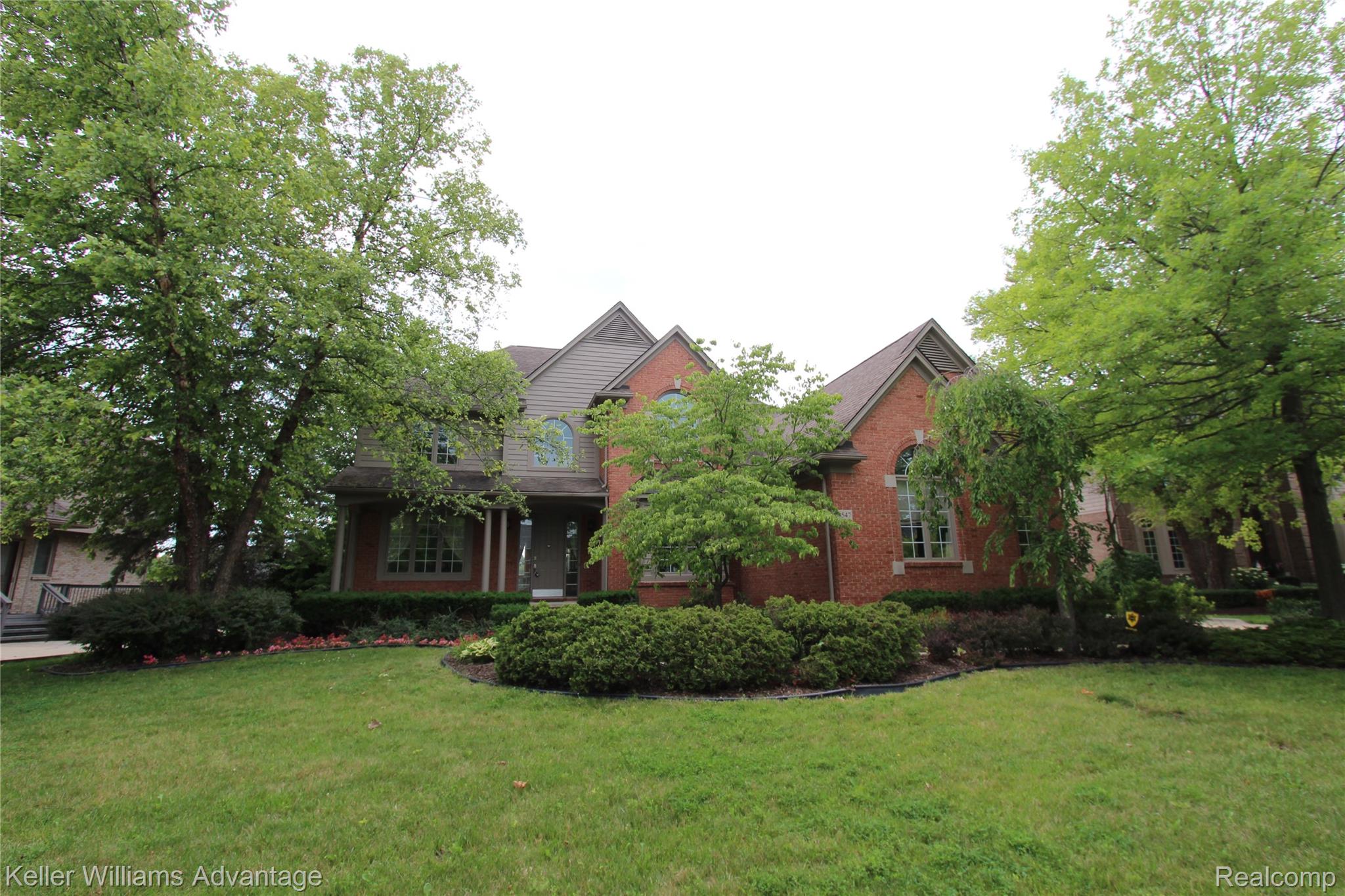 Brick facade residence featuring arched windows and mature landscaping