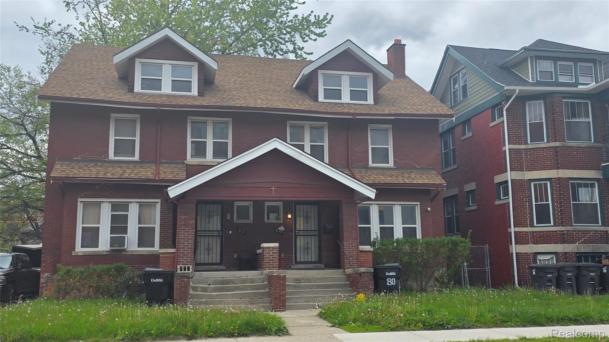American foursquare style home featuring a porch, a chimney, brick siding, and roof with shingles