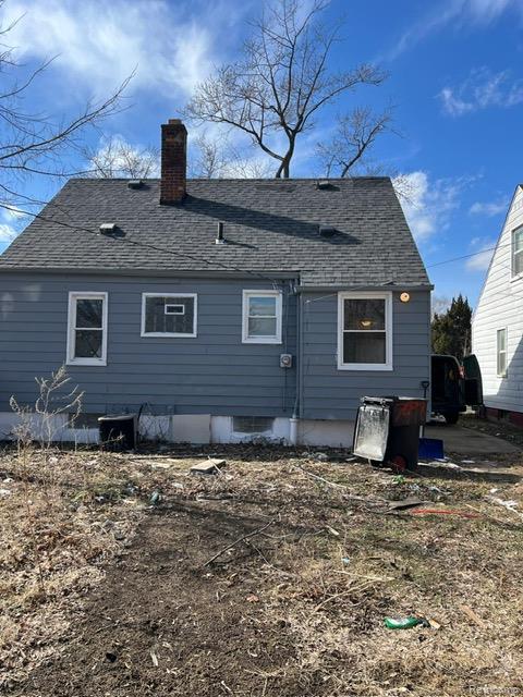 Back of house featuring a shingled roof and a chimney