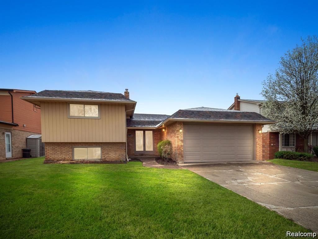 Brick and siding exterior featuring a two-car garage, mature front lawn, and paved driveway