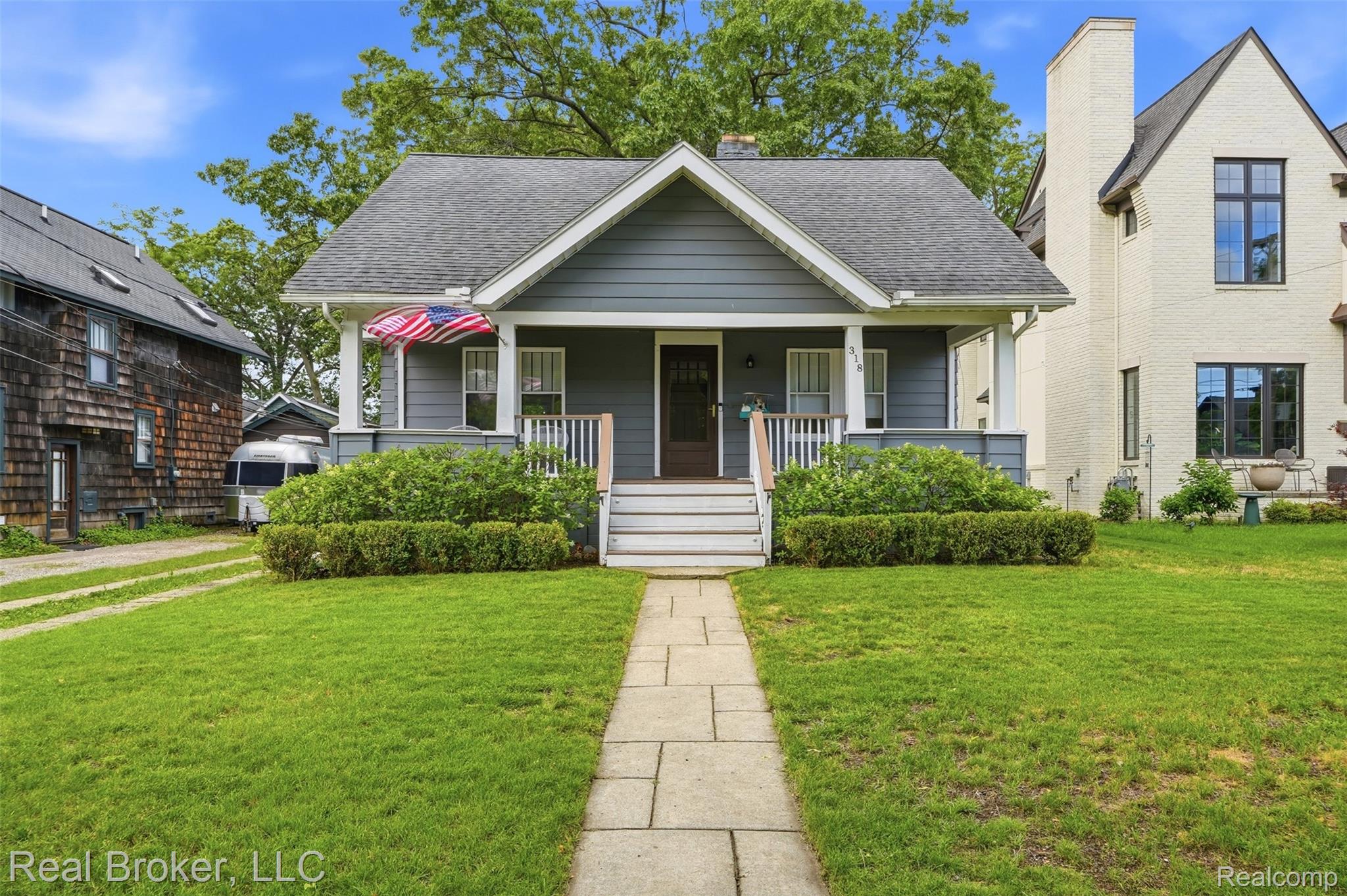 Craftsman-style home featuring a covered front porch with white railings, a dark wood entry door, and a gray siding facade