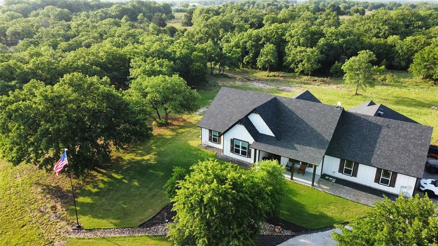This is the one! Modern custom farmhouse on 4.28 private wooded acres backing directly to 400+ acres of LBJ National Grasslands. Enjoy peaceful single story living with a forever backyard filled with mature trees, abundant wildlife, rolling hills, and a seasonal creek. A vast natural setting for hiking and exploring begins right outside your door.
Built in 2023, this 2,689 square foot home features an open concept family room with soaring vaulted ceilings, rustic wood beams, and expansive windows showcasing beautiful nature views. The gourmet kitchen includes quartz countertops, stainless steel appliances, a large pantry, and custom cabinetry with soft close hinges. Luxury vinyl plank flooring runs throughout most of the home.
The spacious primary suite measures 17 by 15 feet and offers vaulted ceilings, dual sinks, and a large walk-in shower with rain head. A dedicated home office or optional dining room adds flexibility, along with exceptionally large secondary bedrooms, including one nearly 19 feet long.
The oversized three car garage provides added depth, epoxy flooring, and strong storage potential. A large vaulted covered patio measuring 20 by 17 feet with epoxy coating creates an ideal space for entertaining. The property also features a gated solar powered driveway entrance and additional visitor parking.
A private water well with a full water purification system ensures quality water. High speed fiber optic internet is installed, with Starlink included as a backup, making it ideal for remote work. The home also includes the remainder of the builder’s structural warranty for added peace of mind.
Located near Alvord with convenient access to the DFW Metroplex, this property combines modern luxury with wide open Texas skies and exceptional privacy.