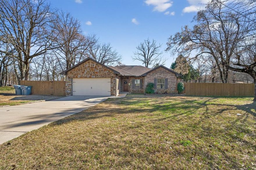 Built in 2023 on 0.43 acres, this 1,522 square foot home offers 3 bedrooms, 2 bathrooms, and a 2 car garage positioned on a spacious corner lot in a rural neighborhood surrounded by mature trees. Step into a welcoming living room highlighted by a tray ceiling and a fireplace that can be enjoyed from both the living area and kitchen, creating a comfortable setting for everyday living and entertaining. The open floorplan is enhanced by LVP flooring and natural light that flows throughout the main spaces. The eat in kitchen features stone counters, beautiful cabinetry, stainless appliances, and generous counter space designed for both busy mornings and relaxed evenings at home. A dedicated laundry room adds convenience and function. The bright primary bedroom offers a private ensuite bath with dual vanities, while additional bedrooms provide flexibility for guests or a home office. Outside, a spacious backyard is shaded by mature trees includes a deck and storage shed, offering room to relax, gather, and enjoy the Texas air. Situated in Gun Barrel City near Cedar Creek Lake and approximately an hour from Dallas, this property combines newer construction with small town charm and easy access to recreation. Cedar Creek Lake is one of the largest lakes in Texas, celebrated for its recreational lifestyle and bass fishing. Proudly Claim Your Piece of Texas!