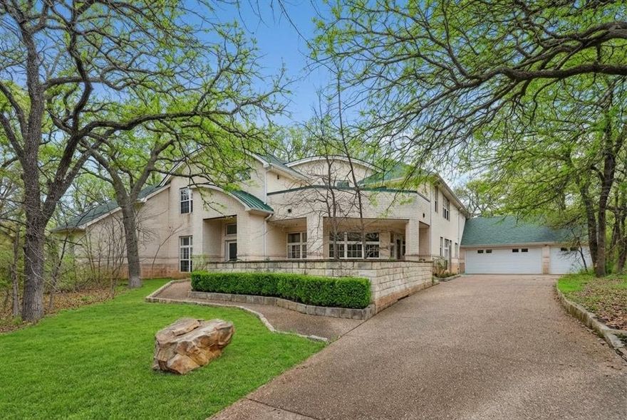 Nestled among mature trees on a peaceful, 2 acre private lot, this distinctive contemporary residence offers a rare blend of character, natural beauty, & expansive living spaces. A sweeping driveway leads to the impressive brick façade & oversized garage, while lush landscaping & serene wooded surroundings create a welcoming sense of arrival. Step inside to a dramatic 2-story foyer where sleek tile flooring, soaring ceilings, & a dramatic staircase immediately set the tone. Natural light pours through windows, highlighting the home’s open & airy design. The spectacular living rm is the centerpiece of the home, featuring towering ceilings, a striking fireplace, & a full wall of windows that frame the picturesque outdoor setting. Elegant columns & a curved second-floor balcony overlooks the space, creating a grand yet inviting atmosphere perfect for both entertaining & everyday living. Architectural details throughout the home—including curved lines, open sight lines, dramatic ceilings, & expansive windows—create a truly one-of-a-kind living experience. The kitchen features warm wood cabinetry w-an abundant of storage pairing beautifully w-sleek quartz counters, a neutral tile backsplash for a clean timeless look, island has add'l prep space, along w-a raised breakfast bar perfect for casual dining. The private office offers a quiet & refined space to work or relax, highlighted by a full wall of custom built-in shelving perfect for displaying books, décor, & personal collections. The expansive primary suite serves as a tranquil retreat, featuring a spacious bedroom w-a tray ceiling, & picturesque views of the lush outdoor setting. A striking wood accent wall adds warmth w-a cozy fireplace. The generous layout easily accommodates a sitting area & provides direct access to the luxurious en-suite bath. This remarkable home combines timeless design, grand scale, & serene natural surroundings—offering a rare opportunity to own a truly unique and captivating property.