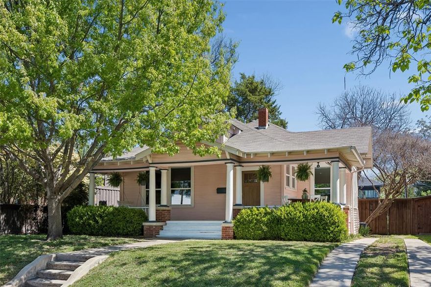Perfectly placed just moments from Bishop Arts District, this charming cottage feels like something straight out of an Oak Cliff storybook—where timeless character meets thoughtful modern updates.

The home’s blush-toned exterior, original stained-glass tulip windows, and inviting wraparound front porch create an unforgettable first impression and embody the relaxed, front-porch lifestyle Oak Cliff is known for. Inside, original hardwood floors, soaring beamed ceilings, pocket doors, and beautifully preserved millwork honor the home’s historic character, while abundant natural light fills the main living and dining spaces.
The reimagined kitchen was designed with both style and functionality in mind, featuring honed soapstone countertops, a farmhouse sink, and an expanded dining area that improves flow for everyday living and entertaining alike. The updated bath offers a fresh yet timeless feel with a renovated shower, updated sink, and marble vanity. Even the laundry and utility room has been thoughtfully redesigned with custom built-ins for added storage and convenience.

Meaningful system upgrades provide peace of mind, including a full electrical rewire completed in 2023, HVAC system replacement in 2023, energy-efficient windows, improved attic insulation, recessed lighting, and charming newer exterior doors.

Outdoors, the home truly comes to life. A newly added approximately 1,000-square-foot back porch and fire pit gathering area create the ultimate setting for entertaining beneath the Texas sky, complemented by a stone patio, refreshed landscaping, privacy fence, and detached storage building.
Warm, inviting, and designed for a lifestyle of casual elegance, this well-maintained home beautifully balances historic charm with intentional modern improvements—all in one of Oak Cliff’s most beloved locations.