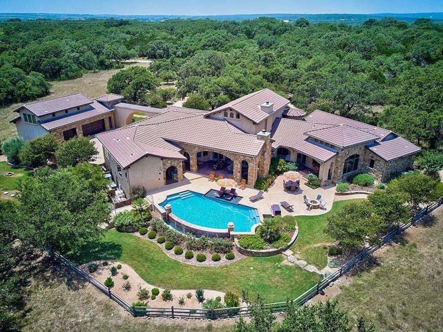 Tucked away within a secluded, gated 20+ acre estate, this exceptional property boasts an agricultural exemption & a meticulously designed 1-story luxury home spanning over 5,500+ sqft, including a detached Casita. A tree-lined driveway leads to the serene property, surrounded by greenery, majestic oaks, open pastures, Hill Country views, & an outdoor living space with kitchen & infinity-edge pool. The residence has 4 bedrooms, 5 bathrooms, a butler's kitchen, media room, study, fitness room, & a dedicated master wing utility room. There's a 2.5-car main garage & 2-story, 3-car garage & shop with a 500 sqft Casita. The property includes a 52,000-gallon rainwater collection system, wine cellar, & high-end kitchen. Conveniently located between San Marcos & Wimberley, with easy access to I-35 & the Hill Country, just 45 minutes from downtown Austin. Students have been accepted into Wimberley ISD, and the renowned San Marcos Academy, a prestigious preparatory school, is just minutes away.