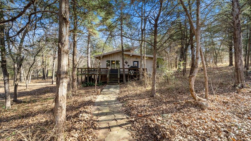 Tucked away among towering trees, this charming 2 bedroom, 1 bathroom cabin in the woods offers the perfect blend of rustic character and modern comfort on 9 MOL fenced acres. The home features an open floorplan highlighted by large windows throughout, creating a warm and inviting atmosphere filled with natural light. Both bedrooms are connected by a Jack & Jill bathroom with a shower & tub combo, and each bedroom is accented with sliding barn doors that add to the cabin’s cozy, country appeal. The living area is anchored by a wood burning fireplace, ideal for cool evenings, while central heat and air and electric appliances provide comfort year round. Step outside to enjoy the open deck, perfect for relaxing and taking in the peaceful, wooded surroundings. A creek winds through the property, complete with two bridges. One for walking and another suitable for a golf cart or small ATV, adding both charm and functionality. Wildlife abounds, making this an ideal retreat for nature lovers. As an added bonus, furniture can be included, along with items in the storage building and two deer feeders depending on the offer. Whether you’re looking for a weekend getaway or full time country living, this secluded cabin offers a rare opportunity to own a peaceful slice of wooded paradise.