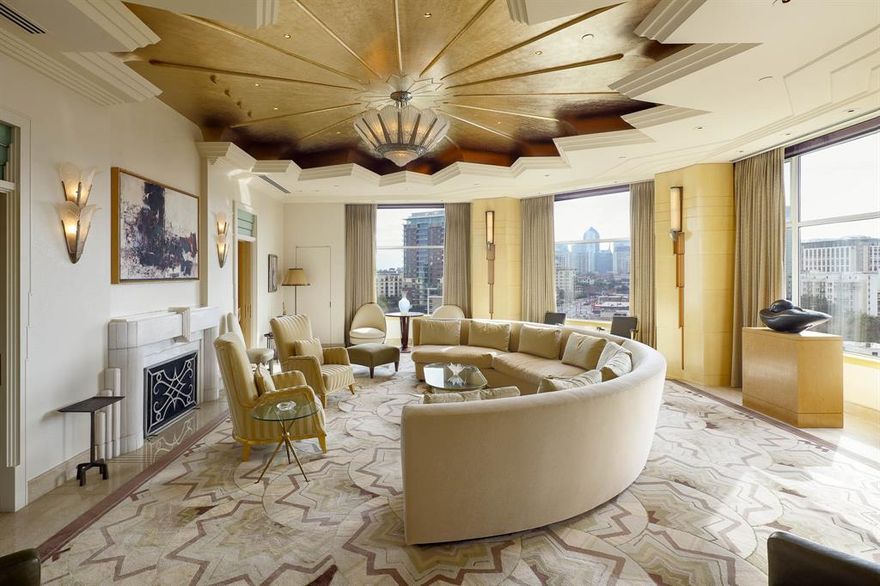 Unit #8W at the Mansion Residences is designed for those who favor the bold. A first look introduces architect Darius Toraby’s concept — 5,302 square feet of Art Deco precision across a grand living room, library, multiple foyers & private terraces. A closer study uncovers the details: brass hardware cast from original molds used at the Paris Opera House, etched glass doors reproduced from Parisian estates, and marble that required three times the typical cutting to achieve perfect book-matching. The living room's gold-leafed cove ceiling frames a 1920 Salerno French light fixture — the very reason the ceiling exists at that height. In the powder room, a glass mermaid panel commands a space designed entirely around it: black marble floors, silver ceiling, and starburst hardware. The library's sycamore paneling was selected to complement specific art, its Roman fireplace finished with bronze end plates. Even utilitarian spaces hold intention. The kitchen's black lacquer cabinets and speckled granite make daily routines feel deliberate. The primary suite's dual bathrooms feature blue mirrored glass and Italian marble, complemented by heated floors and a coffee bar. A second bedroom suite and flexible spaces maintain the same standard: nothing here is an afterthought. Two private terraces — a rarity within the building's exclusive residences — extend living space outdoors with the downtown skyline as a backdrop. Throughout, wall segments are indented for specific art, and rugs are inset into the flooring. This level of specificity promises an invigorating challenge to decorate — but therein lies the reward. As a resident, you inherit twenty-four-hour security, valet, and private access to the hotel's restaurant. This address provides what most luxury buildings only approximate: true hotel-level service in a residential setting. Furniture available for purchase.