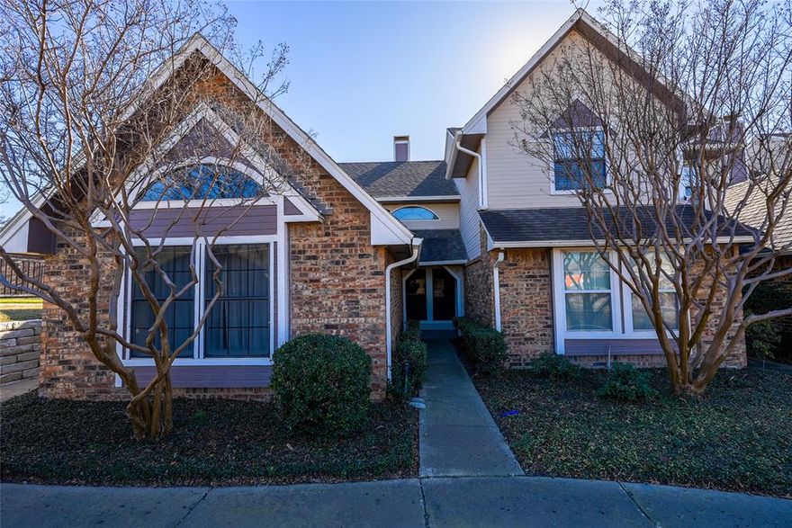 Spacious ground-level condo with functional layout and convenient Carrollton location. Living area features vaulted ceilings, tile flooring, and a wood-burning fireplace. Open dining area connects to the kitchen, which offers ample cabinetry, counter space, and a pass-through to the living room. Primary bedroom includes carpet and ceiling fan with direct access to the full bath. Bathroom offers a tub and shower combination with built-in storage. Covered patio provides additional outdoor space. Attached garage offers secure parking and extra storage. Located near major highways, shopping, dining, and Addison amenities. Property presents an opportunity for updates and customization.