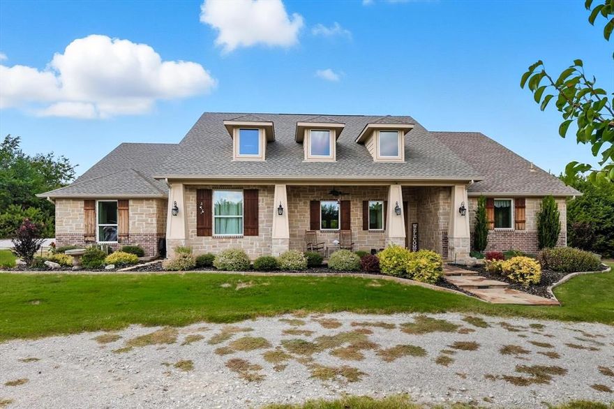 DEVELOPMENT OR FAMILY COMPUND OPPORTUNITY. This home is being offered as a THREE HOME, 15 +- ACRES, OPPORTUNITY IN MELISSA TX. SEE MLS 21078296 AND 21078298
Nestled on a manicured lot with mature trees, this stone and brick ranch-style home welcomes with a covered front porch, gabled roofline, and double-hung windows framed by shutters. Landscaped beds of shrubs and perennials border a flagstone walkway leading to a rustic wood entry door with transom.  Inside, the foyer opens to hardwood floors and a vaulted great room with exposed beams, recessed lighting, and a striking stone fireplace. French doors provide seamless access to the covered patio. Adjacent, the kitchen shines with white beadboard cabinetry, granite countertops, a large center island, stainless steel refrigerator, farmhouse sink under a window, and subway tile backsplash.
The formal dining room features a tray ceiling, crystal chandelier, and expansive windows overlooking the backyard, with built-in cabinetry for storage. Flowing from the living area, a cozy den boasts a second stone fireplace, built-in shelving, and sliding glass doors to the outdoors.
The primary bath impresses with vaulted ceilings, an arched clerestory window, dual vanities on granite counters, white shaker cabinets, travertine tile floors, and a barn-style door. A detached workshop offers a covered porch with cedar posts, ceiling fans, and garage-style doors, set amid a fenced grassy yard with native plantings.