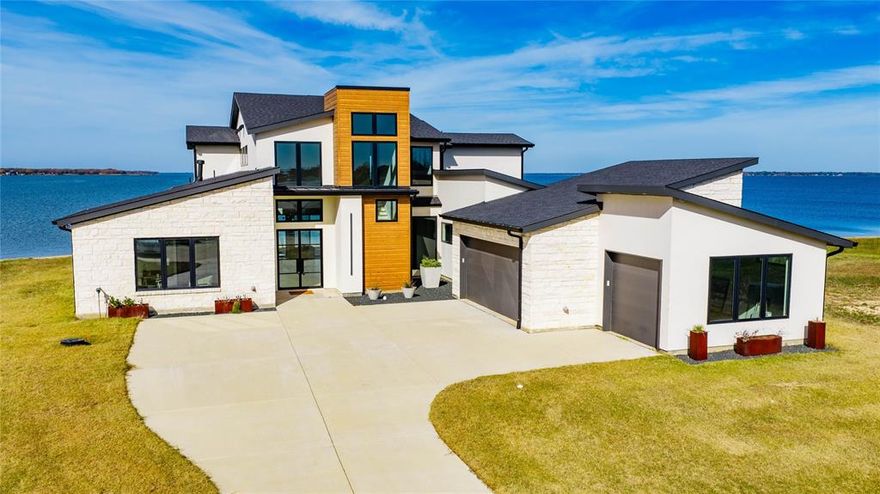 Located in a small, upscale gated community, this contemporary stone and stucco home offers concrete streets and a true luxury lake lifestyle.  The open living area features soaring beamed ceilings, stone fireplace, wood floors, and uninterrupted open-water views.  A chef's kitchen highlights gas cooking, granite counter tops, a large island ideal for entertaining, and an impressive butlers pantry.   The primary suite is a private retreat with raised beamed ceilings, expansive  windows, dual vanities, soaking tub, walk-in shower, and its own coffee bar.  Three additional guest suites, three full baths, a powder bath and a second living area opening to a covered balcony provide space for family and guests.   A covered porch with wood ceilings and exposed beams completes the outdoor experience.  Two boat slips convey with the property at the community marina