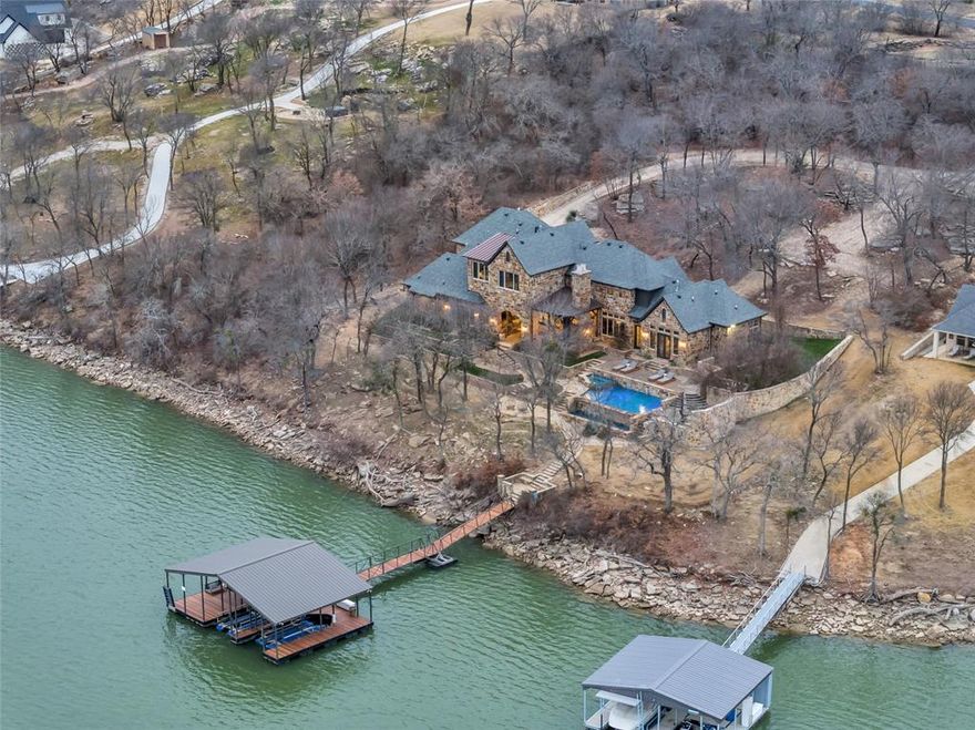 Set on nearly 2 private acres inside a gated community, this extraordinary Lake Bridgeport retreat blends timeless architecture with resort style living and unforgettable waterfront views. Designed to capture the beauty of the lake from every angle, the backyard is a true showpiece featuring an infinity edge pool and spa that appear to spill directly into Lake Bridgeport, expansive stone patios, and multiple outdoor living spaces made for entertaining. The fully equipped outdoor kitchen, paired with a premium sound system, creates the perfect setting for sunset dinners, lake day gatherings, or relaxed evenings under the stars. nside, luxury and functionality meet. The chef’s kitchen is outfitted with a Wolf range, Sub Zero refrigerator, and high end finishes throughout, opening seamlessly into warm, inviting living spaces designed for both comfort and entertaining. The entire home operates on a complete Control4 smart home system, offering effortless control of lighting, audio, climate, and security. Every bedroom is thoughtfully designed as a private primary suite, each with its own full en-suite bath providing ultimate comfort and privacy for family and guests alike. At the water’s edge, the private boat dock features two boat slips, excellent water depth, and a covered seating area ideal for fishing, relaxing, or simply enjoying lake life. With easy access to deep water and protected shoreline, this property offers both beauty and practicality for boating enthusiasts. This is more than a lake house it’s a fully equipped luxury retreat designed for entertaining, relaxing, and making lasting memories on Lake Bridgeport.