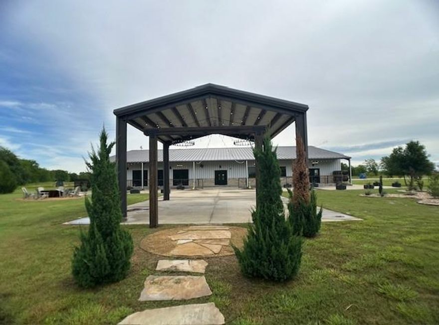 Property is located outside of city limits,  this 12,800 square-foot modern flex space features a variety of uses from a wedding venue (current use), restaurant, dance hall, industrial warehouse, retail showroom, and many more. Inside is an open space with a majestic brick fireplace, a stage, full bar, commercial grade kitchen, four office or storage rooms, and restrooms. On the second floor there is a bridal and a groom suites complete with vanities and private restrooms. It has a staircase that can be used as a grand-entrance.
The outdoor space has a spacious patio terrace covered with awning for events, a fire- pit, a separate metal structure, covered area with arch and a stoned steps to a beautiful pond, as well as other landscaped areas. It has a vast concrete parking lot with a gated entrance. Situated just seconds from I-30, the property is easily accessible by employees and guests , with a maximum capacity of 400 people.