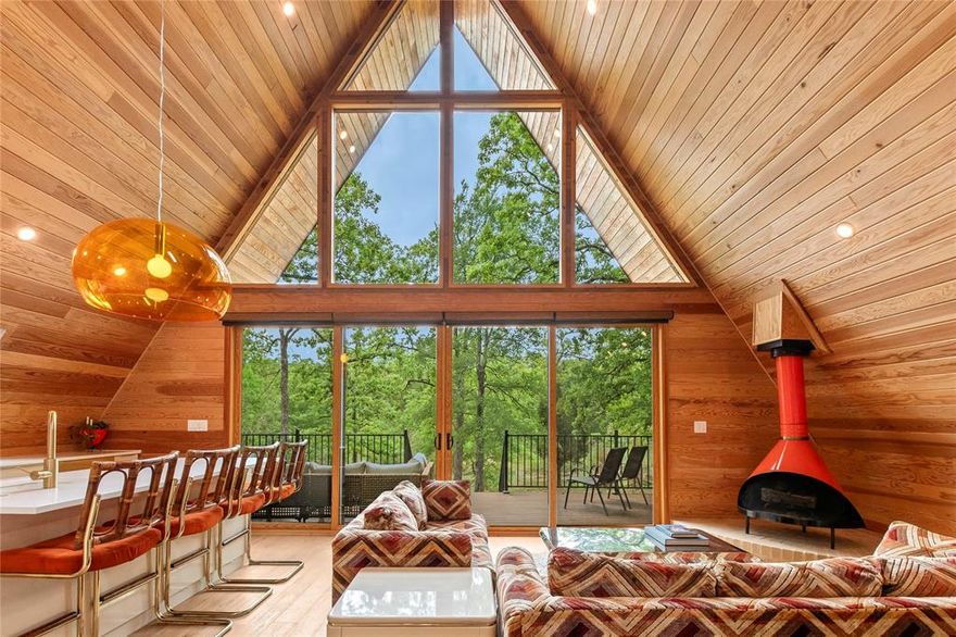 Stunning custom mid-century modern A-frame designed by Kim Lewis and built by Sabado Builders, nestled among mature trees in the lake community of Point La Vista. This architecturally striking home offers 3 bedrooms and 2 bathrooms and backs to a peaceful pond. The open-concept living area showcases dramatic 21-foot Douglas Fir wood ceilings and an expansive water-view window wall with 16-foot sliding patio doors, filling the home with natural light and framed by custom zebra blinds. The space is anchored by an imported vintage Preway wood-burning fireplace and complemented by built-in shelving, creating a warm and inviting focal point. The kitchen blends style and functionality with quartz countertops, bar seating, custom almond cabinetry, a stainless steel dishwasher and range, and panel front built-in Fisher & Paykel refrigerator, creating a seamless and modern aesthetic. The first floor features two bedrooms and a full bathroom with a walk-in shower and terrazzo tile, along with a conveniently located laundry area where the apartment-size washer and dryer convey. Upstairs, the primary suite features soaring ceilings, an ensuite bath with soaking tub, white terrazzo tile, custom windows blinds and an office nook on the landing—ideal for a workspace. Outside, enjoy a concrete driveway with covered parking, fenced side yard with pea gravel area, and tranquil pond views that enhance the home’s peaceful setting. Located in the Point La Vista lake community, residents enjoy amenities including a community pool, frisbee golf course, and boat dock with launch access to Cedar Creek Lake. This one-of-a-kind A-frame blends modern design, nature, and lake living, making it an ideal full-time residence, weekend retreat, or short-term rental opportunity packed with personality! Additional highlights include luxury vinyl plank flooring throughout, custom remote zebra blinds, four mini-split HVAC units, spray foam insulation, transferable starlink internet.