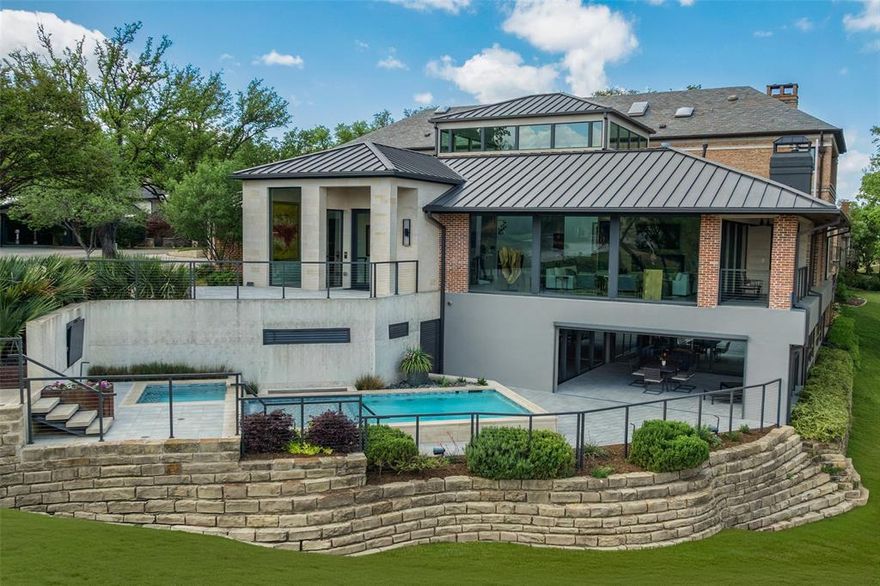 17214 Club Hill is a refined expression of modern luxury, thoughtfully reimagined and expanded in 2020 to nearly 8,964 square feet. Taken to the studs, the residence was rebuilt with all new systems—electrical, plumbing, HVAC, insulation, windows, and roof—and enhanced by integrated Control4 technology for seamless whole-home audio, video, lighting, and security. The interiors are expansive yet composed, defined by floor-to-ceiling Pella architectural windows and multi-slide doors that frame sweeping views across two fairways and White Rock Creek. Level 5 wall finishes, porcelain concrete flooring, custom wood ceiling panels, and stone feature walls create a layered architectural backdrop, while dual floating staircases with integrated lighting serve as sculptural focal points. Linear fireplaces, motorized Lutron shades, and curated lighting further elevate the atmosphere. The kitchen is both functional and beautifully appointed, featuring a large center island, Thermador appliance suite with gas range, double ovens, warming drawer, and dual dishwashers, along with a butler’s pantry and secondary refrigeration. Additional spaces include a wine and whiskey room, media room with 120” screen, game and billiards room, private office, guest suite, and generous laundry and storage. Outdoor living is intentionally layered, with a multilevel pool and spa, firepit, and terraced landscaping positioned to capture the home’s elevated vantage point. Motorized screens create seamless indoor-outdoor transitions, while a circular drive, detached three-car garage, and HOA-maintained grounds offer a true lock-and-leave lifestyle. Bent Tree is entering a new chapter with a 65,000-square-foot clubhouse and a course transformation by Beau Welling. Long recognized as a premier golf destination, the Desmond Muirhead-designed course is being thoughtfully reimagined, complemented by exceptional racquet facilities and a culture of excellence.
