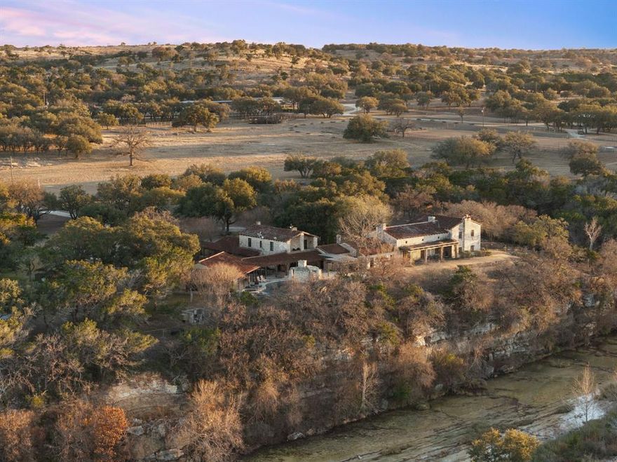 Welcome to Rio Ranchito, a crown jewel of the Texas Hill Country, dramatically positioned along the limestone cliffs of the Guadalupe River in historic Hunt, Texas. This remarkable 168-acre legacy ranch represents refined Western living at its highest level, where luxury, nature, and lifestyle blend seamlessly across a pristine landscape. At the heart of the property is the fully updated six-bedroom, six-bath main residence, a lodge-inspired architectural masterpiece offering sweeping views of the river and surrounding bluffs. The soaring great room showcases exposed timber beams and a massive stone fireplace, creating a warm, inviting space that connects effortlessly to the outdoors. Expansive terraces and tranquil courtyards provide ideal settings for gatherings. The primary suite serves as a private sanctuary with a generous balcony, bath, and breathtaking vistas. Outdoors, an infinity-edge pool and spa visually cascade into the river valley below and are complemented by a fully equipped pool house, perfect for summer afternoons and sunset cocktails. Additional amenities include a game room, private office, gourmet kitchen, and multiple indoor-outdoor living areas designed for effortless entertaining. The newly rebuilt River House features four bedrooms and three baths with contemporary interiors, never-lived-in finishes, and unobstructed riverfront views. Equestrian facilities include a premier 26-stall barn with outdoor arena, round pen, and a barn office with full bath, designed for both serious training and daily care. The ranch also offers an impeccably designed Dog House with twelve individual kennels, custom dog houses, and runs. Supporting infrastructure includes a covered quail barn, hay storage, trailer parking, a charming bunkhouse, a manager’s residence, and two additional staff homes. Whether hosting guests, training horses, or enjoying the Hill Country lifestyle, Rio Ranchito offers an extraordinary combination of luxury, land, and legacy.