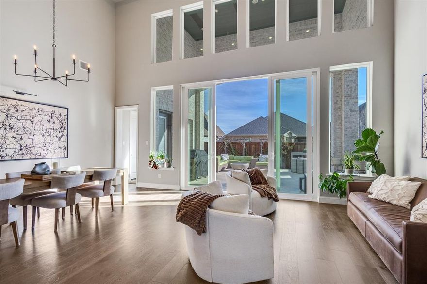 Stunning Highland home in Trinity Falls offering 4 bedrooms, 5 bathrooms, and a 3-car tandem garage with EV charging. This light-filled, open-concept design features white oak flooring, vaulted wood-beamed ceilings, a floor-to-ceiling fireplace, and a dramatic two-story wall of windows with sliding glass doors. The chef’s kitchen includes white cabinetry, quartz countertops, an oversized island, and seamless flow into the dining and living areas—ideal for everyday living and entertaining. Sliding doors extend the living space to a covered patio with gas line for a future outdoor kitchen or firepit, plus landscaped grounds with raised garden beds. The primary suite is a private retreat with a spa-style bathroom featuring a freestanding soaking tub, walk-in shower, dual vanities, and marble finishes. The first floor also offers a dedicated home office, secondary en-suite bedroom, mud bench, and utility room with sink and cabinetry. Upstairs includes two additional bedrooms, a spacious game room, and a separate media room with dry bar—perfect for movie nights or hosting guests. Additional upgrades include tray and vaulted ceilings, mostly 8-foot interior doors, Ring doorbell and camera, transferable Starlink internet, sealed driveway, and custom walkway. Conveniently located near Frazier Elementary and the Trinity Falls amenity center, this home combines thoughtful design, modern upgrades, and access to resort-style community features.