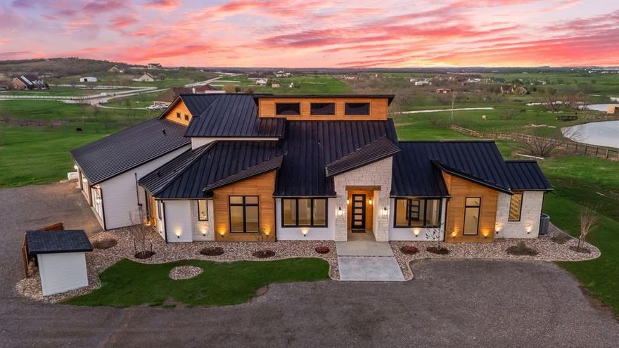 Welcome to this beautifully crafted custom Hill Country modern home set on over 5 acres, offering more than 3,600 square feet of thoughtfully designed living space with breathtaking views of the surrounding countryside. Designed for both everyday living and entertaining, the home features soaring 20-foot ceilings throughout the main living areas, creating a bright and airy open concept layout. The spacious living room showcases a dramatic floor to- ceiling stone fireplace, custom built ins, and expansive sliding doors that open to the outdoor living space. The gourmet kitchen is a true centerpiece, featuring high end appliances, an oversized island, custom cabinetry, and a large walk-in hidden pantry with prep area great for entertaining. The luxurious primary suite offers a peaceful retreat with private patio access, coffee bar,  and a spa-like bath with dual vanities, designer finishes, and a soaking tub. Three large secondary bedrooms each include their own ensuite bathrooms, while a fourth bedroom can easily serve as a private office or flex space. Two additional half baths provide convenience for guests. Upstairs, a spacious game room overlooks the main living area and leads to a large covered balcony—perfect for enjoying panoramic Texas sunsets and wide open views. The covered outdoor living area features a built-in kitchen and grilling space, ideal for entertaining. Built with energy efficiency in mind, the home includes 2x6 construction, spray foam insulation, energy-efficient appliances, and Energy Star-rated HVAC systems for year-round comfort and savings. An oversized garage provides ample space for vehicles, storage, or workshop needs. Enjoy the privacy and beauty of country living while still being conveniently located near town in this exceptional Ponder property.