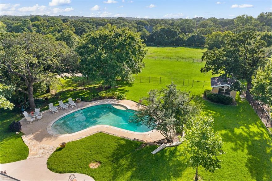 Nestled in the heart of Colleyville, this expansive 2.6-acre estate offers a rare blend of luxury, comfort, and privacy. Surrounded by exceptional homes along Bill Simmons, the property presents a unique opportunity to build your dream residence or enjoy the beautifully maintained one-and-a-half-story home currently situated on the pristine grounds. Inside, light hardwood floors and an open-concept design create seamless flow throughout the main living areas. The inviting living room showcases a striking stone fireplace, custom built-ins, and a wall of windows that frame picturesque views of the lush, manicured landscape. An elegant dining room is complemented by a butler’s pantry featuring a sink and wine refrigerator, leading effortlessly into the chef’s kitchen. Designed to impress, the kitchen is equipped with granite countertops, stainless steel appliances, a commercial-grade gas range, dual sinks, a walk-in pantry, and breakfast bar seating. The spacious primary suite serves as a private retreat with direct patio access and a spa-inspired bath complete with a jetted tub. Outdoors, a covered patio overlooks a sparkling diving pool, creating the perfect setting for entertaining or relaxing in total privacy. A detached workshop adds versatility and functionality to this remarkable property. Zoned R-40, this true Colleyville gem offers convenient access to DFW International Airport, Highways 121, 114, and 360, and is just minutes from premier shopping and dining in Colleyville, Grapevine, and Southlake, with Dallas and Fort Worth a short drive away.