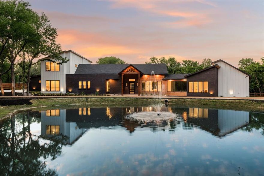 There’s a sense of calm the moment you arrive—when the trees give way and the pond comes into view, glassy and still, mirroring the sky. Set on nearly two acres in the heart of Bartonville, this newly built five-bedroom home offers the rare balance of peaceful seclusion and everyday convenience. It feels private, quiet, grounded—yet you're minutes from everything.
At first glance, the architecture draws you in. Clean lines. Natural materials. A sense of ease. Then you notice the bridge—glass, elegant, unexpected—stretching over a winding creek and leading to the master suite and office. It’s a design that blurs boundaries, both literally and figuratively. Indoors and out. Work and rest. Structure and nature.
Inside, the home unfolds in a way that feels intentional. Light floods every room. Large windows frame the surrounding trees. Every view, curated by the land itself. The kitchen is warm and functional, designed for both daily living and effortless hosting—with a hidden butler’s pantry that keeps the rhythm of life moving smoothly behind the scenes.
The heart of the home flows outward. Expansive outdoor living spaces invite you to linger—multiple patios tucked into the landscape, each one offering a different perspective. Morning coffee. Evening gatherings. Late-night stargazing.
The master suite is a retreat, removed from the main living spaces just enough to feel like your own sanctuary. The office sits nearby, perched above the water with calming views of the pond—a setting that brings focus without effort.
Built by the visionary team at Highpoint Homes, every inch of the property has been thoughtfully considered. From the mature trees that offer shade and presence, to the pond that anchors the land in quiet beauty, this is a home that lives differently. A place to slow down, breathe deep, and still be close to what matters.