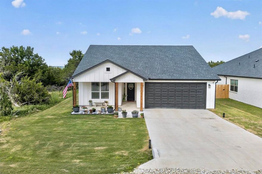 Modern farmhouse with a great layout & scenic lake views sitting on over a quarter of an acre! Located in a gated community nestled along Lake Granbury, residents of Canyon Creek enjoy a LOW HOA with access to multiple pools, tennis + basketball courts, a playground & private boat launch. Built in 2024, this like-new home is packed with perks. Step off the sizable covered front porch into an open floor plan filled with natural light pouring in from oversized windows throughout. Kitchen is complete with quartz counters (sturdy yet sleek), a large island, SS appliances & tons of cabinet storage. Full laundry room conveniently located right off the kitchen. Split bedroom layout makes for a highly private primary suite, featuring vaulted ceilings & a gorgeous ensuite with dual sinks, a Hollywood tub, glass shower & massive walk-in closet. Outside, an expansive backyard boasts beautiful views of the lake & great space for entertaining or relaxing! The sellers have further enhanced this outdoor setup by extending the back patio & fully enclosing the backyard with wrought iron fencing. PLUS, this home offers an oversized 2-car garage, perfect for larger vehicles & added storage space. Situated along a quiet cul-de-sac, minutes from tons of outdoor activities including easy access to Harbor Lakes Golf Club, local fishing spots, neighborhood sport courts, boat slips & more. Come see everything lakeside living has to offer!