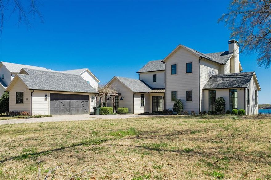 This stunning modern farmhouse sits on an elevated 1 acre lot, offering panoramic lake views and 112 feet of shoreline.  Designed for effortless living and entertaining, the open-concept layout features high-volume beamed ceilings, a cozy wood-burning fireplace , and wood flooring throughout.  The dream kitchen is a show stopper with its soft, calming color palette, quartz countertops, painted cabinetry, Bertazzoni range, island with seating, and a well appointed beverage center complete with refrigerator. Enjoy two luxurious primary suites on the main level, each with serene lake views.  Upstairs you'll find two additional guest suites, a second living area, and a flexible space perfect for sleeping accommodations or a game area.   Relax and entertain on the expansive covered porch - ideal for outdoor dining, lounging by the fireplace, or simply taking in the view.   The large boathouse offers everything your need for lake life, including boat and personal watercraft storage, plus a spacious sun deck