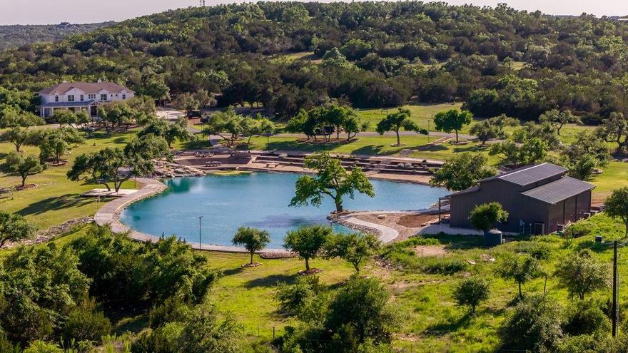 25-acre hill country estate in Driftwood. Resort-style haven with privacy, panoramic views, & wildlife exemption. Its focal point is a 1-acre pond with trails, a waterfall, dock, beach, & deck. Adjacent is a custom outdoor kitchen. Two barndos grace the grounds. 6,000 sqft custom home features French white oak floors, a wine room, wet bar, & flawless kitchen. Main level includes a breakfast room, media-game room, guest room, office, & dog room. Upstairs, enjoy views, a gym, & a lavish master suite. Outdoors, an entertainer's paradise awaits with a pool, hot tub, patio, & kitchen. Also included are a trampoline, sports court, & park-like area. One barndo boasts smart technology, reclaimed brick, & a custom kitchen, the other accommodates 30 cars & features reclaimed brick & glass doors. There's also a vegetable garden & a chicken coop, irrigation, water tanks, wells, & Starlink Internet. Zoned for Dripping Springs ISD. Natural beauty & upscale amenities for luxury living.