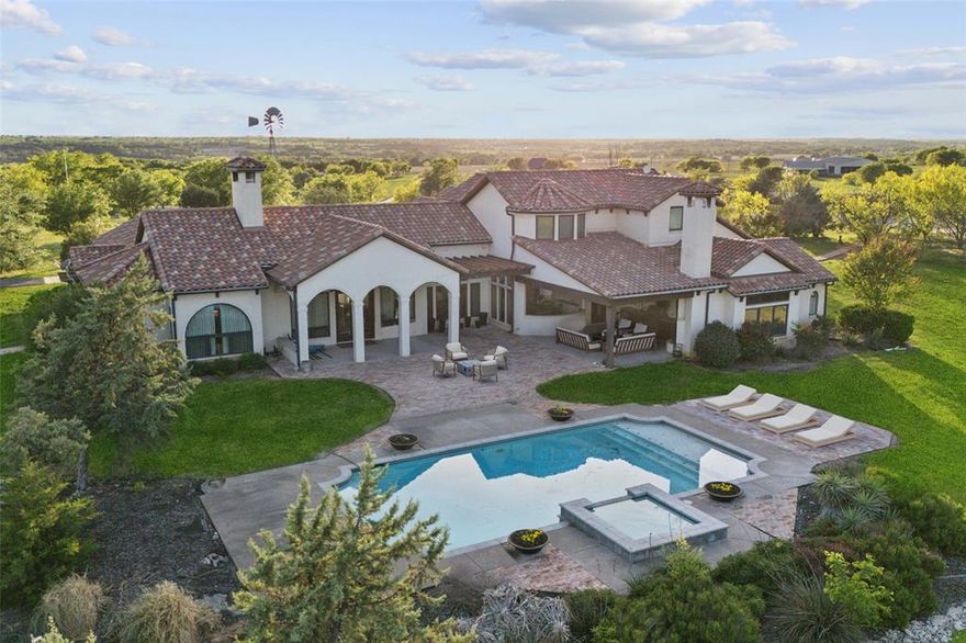 Unparalleled Opportunity: 3-Acre Luxury Estate with Limitless Potential Near Future Bluejack Ranch Golf Course. Perched atop one of Aledo’s highest hilltops, this extraordinary 3-acre estate offers a rare combination of luxury, privacy, and boundless opportunity—with no HOA restrictions. Welcome to Fossil Rock Ranch, an elegant Mediterranean-inspired masterpiece thoughtfully designed for entertaining and refined living. Located just minutes from the future Bluejack Ranch Golf Course—a world-class development by Tiger Woods—this prime location is a once-in-a-lifetime opportunity for investors, developers, or avid golfers seeking a trophy property with income-generating potential. Imagine transforming this spectacular land into a luxury golf retreat, wellness resort, Airbnb compound, exclusive bed & breakfast, or a private multi-generational family estate. With rolling pastures, panoramic views, and 4 adjacent water wells, the possibilities are as expansive as the land itself. The custom-designed main residence is a true showpiece of craftsmanship and style, featuring white oak and brick flooring, custom doors and windows, a gourmet chef’s kitchen with professional-grade appliances, a built-in refrigerator, granite countertops, and a butcher block island. The grand living room boasts vaulted, beamed ceilings, twin drop-down chandeliers, and a stunning stone fireplace, creating the perfect space for entertaining. Step outside to a resort-style backyard with multiple patios, mature trees, an outdoor fireplace + a sparkling pool overlooking endless Texas skies. The Primary Suite offers a serene retreat with a spa-inspired bath, sauna, private outdoor shower, walk-through closet, and personal workout room. Additional highlights include a separate barn currently being transformed into a barndominium for future living quarters, offering unmatched flexibility for future development or personal vision. An Additional 97 acres are available!