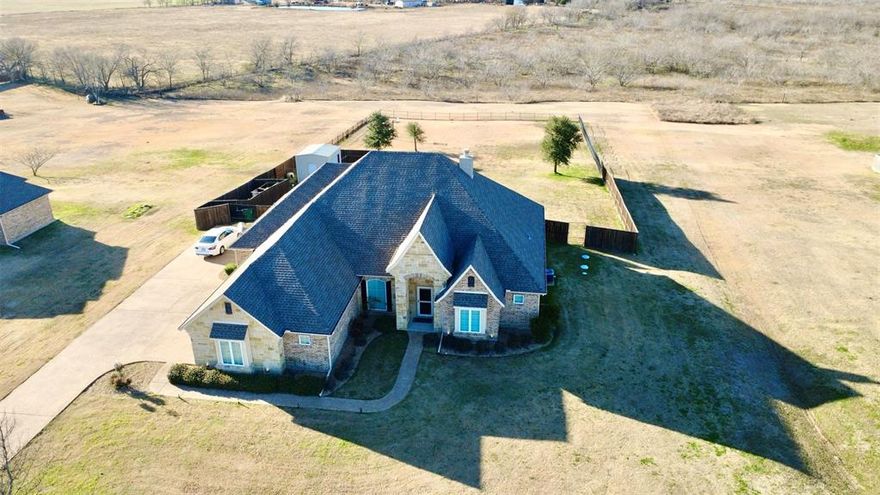 Welcome to your dream home just outside Kaufman, Texas — where custom craftsmanship, modern elegance, & wide-open Texas living come together in perfect harmony. This stunning custom-built residence sits on over an acre of land that extends well beyond the large, fenced yard. It features 3 bedrooms, 2.5 baths, a dedicated home office, 2 dining areas, 2 living areas, & a spacious 3-car garage. The Tudor-inspired exterior boasts beautiful natural stone accents, an extended aggregate drive, & a solid wood speakeasy front door that makes a lasting first impression. Inside, rich ceramic tile with the look of hand-scraped wood flows throughout the home, creating warmth & continuity. The inviting living room centers around a huge stone fireplace, while two dramatic sliding barn doors with translucent glass panels open to reveal a flexible bonus room, perfect for a game room, home gym, or media retreat. Crown molding can be found throughout the home as well as stylish wooden shutters! The chef’s kitchen features a beautifully veined marble island, custom cabinetry, stainless-steel appliances, & elegant pastel tile backsplashes set on the diagonal. The primary suite is a peaceful retreat, complete with a tray ceiling & a luxurious en-suite bath with oversized tub, walk-in shower with custom tile, & dual vanities. Step outside & discover your personal resort, a custom pergola overlooks a sparkling pool & spa, surrounded by the tranquility of open Texas countryside. A powered metal shop provides the perfect space for hobbies, storage, or projects. Located within highly rated Kaufman ISD, this home offers convenient access to major employers, shopping, dining, & nearby highways, making commutes simple while preserving the serenity of country living. Here, you’ll experience the best of both worlds, the peace of small-town TX life & the sophistication of a truly custom-built home. Schedule your private showing today & see why this Kaufman gem is one you’ll want to call your own.