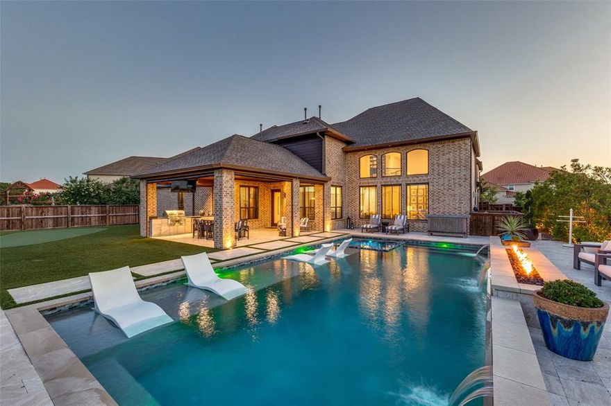 Timeless architecture and refined upgrades come together in this exceptional Frisco estate, where every space is custom-crafted for beauty, comfort, and entertaining. Inside, soaring ceilings and walls of windows flood the living room with natural light, accented by a statement fireplace, custom built-ins, and graceful archways. A sweeping staircase in the foyer sets a dramatic tone, while wide-plank hardwood floors and designer lighting carry throughout. The open-concept kitchen is a dream: anchored by a quartz island, 6-burner gas range, double ovens, & sleek white cabinetry. A richly appointed office with soaring ceilings and a full wall of custom bookshelves overlooks the front drive. Between the office and living room, a bespoke bar room includes wine wall racks, humidor, wine fridge, and brass open shelving—speakeasy vibes. The spacious primary suite is a true retreat, complete with separate his-and-hers closets and a spa-like bath. An additional bedroom and bathroom downstairs makes for the perfect mother-in-law suite. Up the casual back staircase, you will find oversized secondary bedrooms each feature large walk-in closets, while the game room with custom built-in study area and a media + fitness room offer abundant flexible living spaces. Step into a private outdoor paradise designed to rival any luxury vacation. A resort-style pool with waterfall and fire features, lounging deck and spa, surrounded by turf + a putting green adds playful charm to the grounds.The expansive covered patio is an entertainer’s dream: full outdoor kitchen, mounted TV, and designer dining area—all under an elegant ceiling with Bromic heaters that keep the space toasty year-round. With the press of a button, motorized screens lower to create a completely bug-free, climate-controlled environment—so you can enjoy outdoor living in all seasons, day or night. Additional highlights include a 4-car epoxy-finished garage, oversized laundry with custom cabinetry, & fire sprinkler system.
