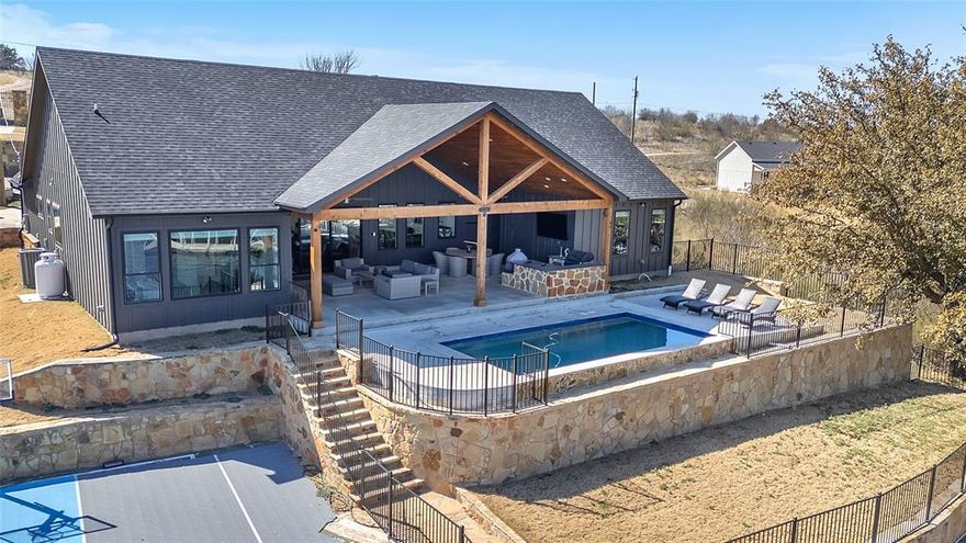 Welcome to your dream lakefront home! This stunning new property boasts a modern open floor plan that seamlessly blends luxury, comfort, and tranquility. Nestled in a quiet cove, it features a private dock, a sparkling pool, and a basketball court—perfect for an active family seeking the ideal home away from home. As you walk through the front door, your eyes will be drawn to the wall of glass that frames a breathtaking view of the serene swimming pool and the calm lake beyond. The open concept living, dining, and kitchen area is bright and welcoming, offering a perfect space to unwind after a long day. Two large glass sliders lead to a spacious outdoor patio with vaulted wood plank ceilings. Here, you can enjoy your favorite sporting events on the large outdoor TV while grilling or lounging by the pool. Dine or play cards at the large round outdoor table, all while taking in the stunning views. The master suite is a sanctuary with a wall of windows overlooking the pool, basketball court, and quiet cove. Wake up to beautiful sunrises over the cliff wall from the comfort of your bed. The master bathroom features two separate vanities, a soaking tub, a walk-in shower, and a separate toilet room. A second king bedroom is located next to a full bathroom with a walk-in shower, while two additional bedrooms each feature two queen beds and share a bathroom with a double vanity, walk-in shower, and separate toilet area. The two-car garage with separate access to the upstairs suite with two queen beds and a full bathroom is approximately 420 additional sqft, making the property a 5 bedroom, 4 bath. This beautiful home offers everything you need for a life of luxury and relaxation by the lake. Don’t miss the opportunity to make it yours!