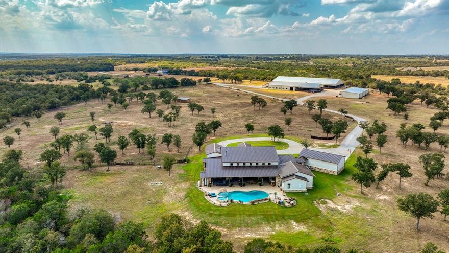 Nestled in the rolling hills of Mineral Wells, this remarkable 69± acre estate combines refined luxury with the serenity of wide-open Texas ranch land. At its center stands a custom 6,114± square-foot residence, thoughtfully designed with five bedrooms, five full bathrooms, and two half-baths. Every detail has been carefully curated, blending rustic elegance with modern convenience. Inside, you’ll find expansive living spaces anchored by a dramatic rock fireplace and soaring wood-beamed ceilings. The chef’s kitchen is a true showpiece, featuring premium appliances, dual dishwashers, a spacious pantry, and a functional layout designed for both entertaining and everyday living. You'll love the butler's pantry that provides additional storage. A wall of windows brings the outdoors in, connecting seamlessly to the back patio and sparkling pool, where sweeping views of the surrounding countryside set the stage for unforgettable gatherings. The master suite is a private retreat, complete with its own stone fireplace, spa-inspired bathroom, and an oversized closet with custom finishes. Additional bedrooms are equally well-appointed, offering comfort and privacy for family and guests alike. Beyond the home, the ranch is built for both leisure and function. Rolling pastures, mature trees, and ample space provide endless opportunities for recreation, livestock, or hay production. There is a seasonal creek that run through the property. The property also features a 125' x 250' covered arena-perfect for any discipline, an 18-stall horse barn, and a Priefert walker, making it ideally suited for any equine needs. This estate offers a rare combination of luxury, seclusion, and versatility—just minutes from Mineral Wells and within easy reach of the DFW Metroplex. This house is a rare find! It was recently featured in the Cowgirl Magazine!