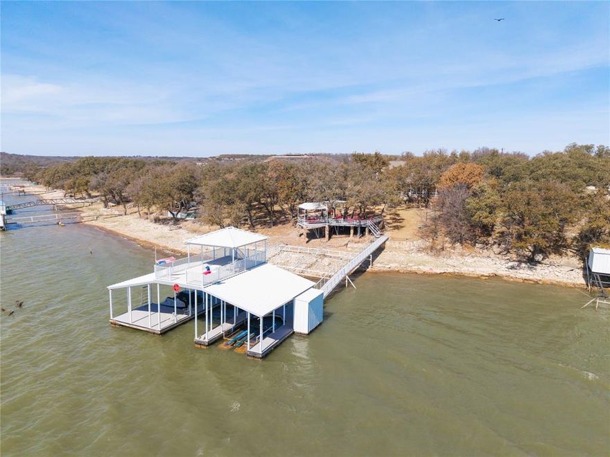 Deep-watered, fully-furnished Dominion Point lake-front home on beautiful Lake Brownwood! Bring all the family and friends! There's plenty of room with five bedrooms, three baths and lots of outdoor entertaining areas including a spacious composite-board deck cantilevered over the water. The fully-landscaped yard - completely shaded by mature live oaks - includes a sprinkler system, built-in gas grill and 12' x 12' storage building with covered chain-linked fenced dog pens. And the gently-sloping flagstone walk provides easy access to the 30' x 48' two-slip aluminum dock with Hydro-Hoist lift, two floating jet ski ports, roomy storage closet and 17' x 30' covered sun deck. The dock floats in an estimated 18 to 20 feet of water when the lake is full. The two-story rock home includes three bedrooms (including the primary), two baths, living-dining, wood-burning fireplace, kitchen and utility room downstairs complimented by two bedrooms and a jack-n-jill full bath upstairs. All three downstair bedrooms open through French doors to a covered flagstone porch and scenic easterly views of the lake. The primary and guest baths downstairs include granite counter tops with tiled counter tops in the kitchen. The living area, kitchen, bathrooms and utility are floored in ceramic tile and all five bedrooms are fully carpeted. Park your car and golf cart securely in the two-car attached garage with electric door opener. Come home to this inviting lake-front property and stay awhile. Slow down, take your shoes off and enjoy the quiet serenity of lake living.