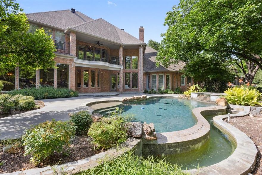 Tucked away in a peaceful cul-de-sac that backs to scenic walking paths and a tranquil community pond, this beautifully crafted 5-bedroom, 5.5-bathroom home offers 5,414 square feet of luxurious living. From the moment you enter, you’re greeted by soaring ceilings, intricate millwork, and timeless finishes. Just off the entryway, a handsome office or library with built-in shelving provides a quiet, sophisticated space for work or reading. The formal living room features a grand fireplace flanked by architectural niches and tall windows that flood the space with natural light. The heart of the home is the well-appointed kitchen, designed for both function and style. Rich wood cabinetry, granite countertops, a custom vent hood, and a central island make this space ideal for the home chef. Just off the kitchen, a built-in wine cellar provides the perfect environment for storing and displaying your collection, making it a seamless addition for entertaining. The adjacent informal living room and breakfast area offer inviting spaces for everyday living, while the formal dining and living rooms provide elegant options for hosting. The first-floor primary suite serves as a luxurious retreat, complete with serene views of the backyard and a spacious spa-like bathroom. Built-in cabinetry throughout the home adds an abundance of storage, and the oversized laundry room offers added functionality and organization. Upstairs, a generous game and seating room offers a versatile space for recreation, media, or relaxation. Step outside to your own private oasis where a lush, park-like setting surrounds a sparkling pool with waterfall features and integrated spa. Mature landscaping, curved stone edging, and multiple patio areas create a peaceful atmosphere for outdoor living and entertaining. With direct access to scenic walking trails and a community pond just beyond the backyard, this home offers a rare blend of luxury, comfort, and natural beauty.