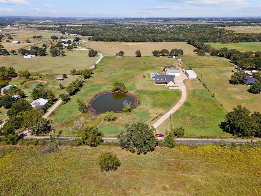 A blend of country living with modern convenience. Minutes from the Chisolm Trail, and a Texas favorite HEB. On over 7 acres of serene countryside, this fully fenced property offers privacy and space for projects, toys or a business. A spring-fed pond enhances the setting as you enter the property, while the Prairie-style home sits atop the long driveway. The home offers a warm welcome with its open floor plan. Tile floors span the home, and plantation shutters let the light in. With 3 bedrooms and 2.5 baths the well-planned layout is comfortable. The third bedroom, currently used as an office, features a built-in Murphy bed for added functionality. The heart of the home is the kitchen, which opens to the living room with 19-foot ceilings and custom cabinetry. The kitchen is equipped with a large built-in pantry which is almost hidden and adds great storage. For those who value storage and workspace, the property features two large shops. The first, approximately 2,000 square feet is 70x26, includes six car bays and a 200-amp service, perfect for automotive projects. The second shop, measuring 50x40, is equally impressive with an air-conditioned craft room, workout room, bathroom, and laundry space with stackable washer and dryer. A second-level deck adds versatility.

Outdoor living is highlighted by a large, 20x50 diving pool with a 10-foot depth. Additionally, a storm shelter is positioned perfectly on the property for access and safety. Tucked out of sight is a dog pen with an 18-inch footer and high fence. The home is connected to city water with the additional benefit of a 660-foot depth well. The home has spray foam insulation and was painted with Rhino Shield in 2023 and also a newer roof and gutters. The house is equipped with a plumbing manifold and two hot water heaters. There is a REME light air purification system. The built-in cabinets in the living area are fitted for a fish tank.