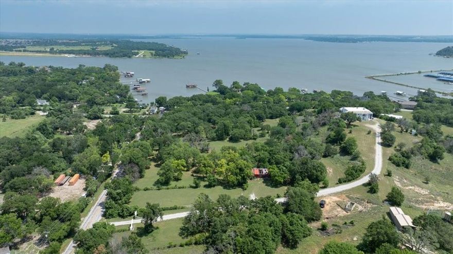 This land provides you the most amazing full views of Eagle Mountain Lake and is located just 2 minutes from Eagle Mountain Marina on Wells Burnett Road. Enjoy the beautiful daytime views of the lake and peaceful lake and harbor lights visible at night providing a fully relaxed lifestyle. 
Sitting on top of the hill is a large home built in 1975.  The seller understands that the home needs a full remodel but the location of the home provides full views from the second floor large back deck off the large primary bedroom. Amazing views are also visible from the front and side yard as well as well as views of downtown Fort Worth on a clear day.  The home does have 4 bedrooms all with ensuite bathrooms - 1 bedroom is located on the first floor.  There are two beautiful stone fireplace walls, one in the great room and one in the primary bedroom.  There is a well and a septic system and more wells could be be drilled with a minimum of two acres per well if the new owner wanted to build additional family homes.  This land could also be used for a small development. Azle city water and sewer are close by but not on the property.  There are so many opportunities for a new owner and animals are allowed.  The same family has had ownership for nearly 50 years.  A new survey done in April 2025 is available.