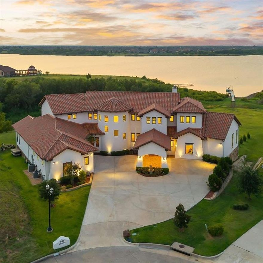 Experience luxury lakeside living at its finest. This 6,316 sq ft custom-designed estate offers an unmatched blend of elegance, comfort, and resort-style amenities perfectly positioned on the tranquil shores of Lake Lewisville. Enjoy panoramic lake views from nearly every room, and wake up each day to breathtaking sunrises, abundant wildlife, and the peaceful rhythm of waterfront living, all just minutes from city conveniences.
Inside, soaring 26-foot ceilings, hand-selected finishes, and walls of windows frame the expansive living spaces. The chef’s kitchen is fully equipped with premium appliances, including two Miele dishwashers, a DCS range, Liebherr refrigerator and freezer, and a walk-in pantry and seamless flow to the open-concept entertaining areas. The primary suite is a true retreat with a spa-inspired bath and a custom storm-shelter walk-in closet.  2 Additional en-suite bedrooms downstairs, a private studio with exterior access, and an artistic wine cellar add both function and flair.
Upstairs, enjoy a game room with full bar, home theater, and two additional bedrooms, including one designed as a dedicated gym and another with its own private terrace and pergola.
Step outside to your private oasis. The meticulously manicured grounds are a testament to proud ownership! Enjoy the koi pond with waterfall, rustic gazebo, three-hole putting green, and 130 feet of direct lake frontage with a private dock, perfect for boating, fishing, or sunset views. The 4-car collector’s garage includes space for lifts and a professional workshop. Built with 18-inch walls and envelope insulation, this home is not only stunning, but energy-efficient.
This is more than a home, it’s a lifestyle. A rare opportunity to own a one-of-a-kind lakefront estate in one of the most desirable areas of DFW.