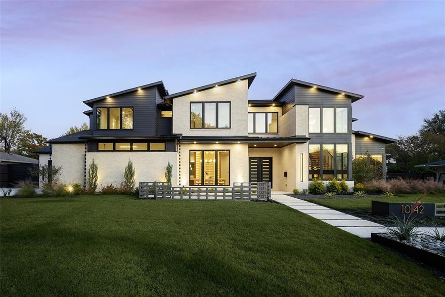 10142 Coppedge Ln, is a new-construction mid-century transitional showpiece by Chris Sandlin Homes on a 0.35-acre lot in the coveted Private School Corridor. A striking façade of light brick and charcoal siding with crisp gables, modern paver walk, and sculptural succulent planters sets the tone. Inside, wide-plank floors lead to a vaulted great room framed by clerestory windows and an expansive wall of sliders to the backyard. Custom walnut millwork with integrated lighting flanks a sleek linear fireplace and floating hearth, creating a refined focal point. The entertainer’s kitchen pairs a dramatic veined-marble waterfall island and matching hood with bespoke walnut cabinetry, brass hardware, and stacked-tile backsplash; a brass-and-glass bar wall with beverage refrigeration and a walk-in pantry complete the space. A show-stopping office wrapped in cobalt blue features steel-and-glass doors and floor-to-ceiling walnut built-ins. All bedrooms are ensuite, and two generous laundry rooms add everyday ease. The serene primary suite offers a wood-cased niche with cove lighting, sitting area, and direct yard access; its spa bath indulges with a freestanding tub, oversized glass shower, dual vanities set in walnut cabinetry, designer lighting, and brass fixtures. Secondary baths are equally curated, from a jewel-box powder with indigo-and-gold wallpaper and black vessel sink to a guest bath with glossy elongated-hex tile, terrazzo floor, and pendant lighting. Outdoor living shines with a large covered terrace—tongue-and-groove ceiling, recessed lights, fans, and a built-in grill—overlooking a pool-sized lawn wrapped by a modern privacy fence. A rare fusion of custom craftsmanship, natural light, and timeless style, minutes from Dallas’s top private schools.