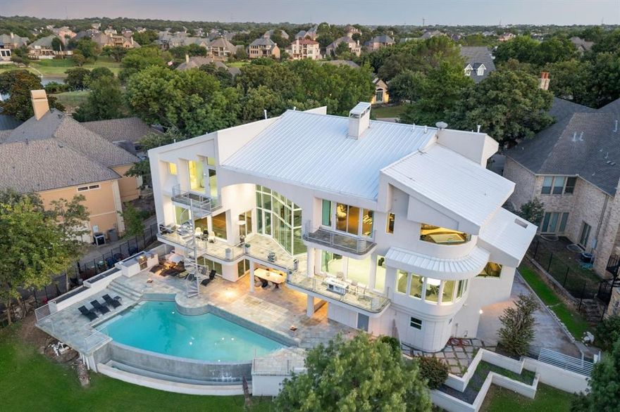 Where cutting-edge design meets the serene beauty of the water—this ultra-modern lakefront estate delivers a lifestyle like no other. Perfectly positioned on a quiet cul-de-sac and spanning an impressive 179 feet of pristine Lake Lewisville shoreline, this three-story, 8,553 sq ft showpiece offers sweeping, unobstructed lake views from nearly every room. From the moment you step inside, 30-foot ceilings and walls of commercial-grade glass frame the ever-changing blues of the lake, blurring the lines between indoors and out. Architectural artistry shines in the dramatic floating staircases, multiple view-drenched balconies, lighted art niches, and a striking floor-to-ceiling glass wine display. Designed for both grand entertaining and private escapes, the home features 4 bedrooms, 5 full baths plus a half bath, a study that could also be utilized as a 5th bedroom, media room, game room, gym, and an indoor heated spa with dry sauna. The main level hosts a chef’s dream kitchen with granite countertops, professional-grade stainless appliances, 6-burner gas cooktop, double ovens, and a Sub-Zero built-in refrigerator. The owner’s retreat is a sanctuary of its own, complete with a private balcony where you can savor sunrise over the water and end your day with mesmerizing sunsets. Outside, resort-style amenities abound—an infinity-edge pool that seemingly spills into the lake, an outdoor kitchen with grill, and multiple covered patios perfectly oriented for entertaining against a breathtaking backdrop. Energy-efficient features, a durable metal roof, and meticulous maintenance ensure this residence is as functional as it is beautiful. This is more than a home—it’s a front-row seat to the most spectacular views Lake Lewisville has to offer, and the pinnacle of waterfront luxury living.