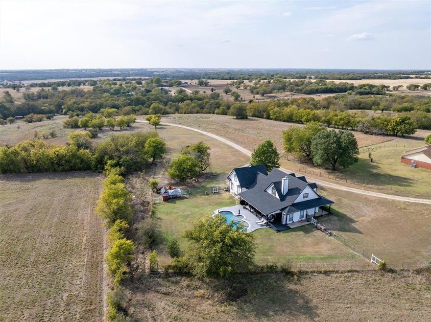Modern Farmhouse on gated 2 acres with newly remodeled pool and stunning countryside views. This beautifully remodeled 4-bedroom, 2.5-bath modern farmhouse blends charm and function on serene acreage. The open living area features lofted ceilings, wood beams, rich hardwood floors, and a cozy stone fireplace framed by expansive windows and a set of doors that overlooks the pool and countryside beyond. The kitchen has the perfect pristine white glass front cabinets, a large farmhouse porcelain sink, palette pleasing granite, comfortable large island, and convection oven with pot filler. The primary suite opens directly to the patio and pool and includes a spa-inspired bath with dual sinks, seamless glass shower, and dual shower heads. A large 15x14 secondary bedroom and powder bath completes the first floor. Upstairs are two spacious bedrooms, a beautifully updated full bath, and a large 26x13 game room - movie room - second living - office accessed by a separate rear staircase. Outside, enjoy the wide covered patio, newly remodeled pool, and peaceful views. The current owners enjoy their chicken coop, friendly goats, and neighboring cows, all adding to the charm of this private country retreat with shared gated access and a long private drive—true country living just minutes from town conveniences.