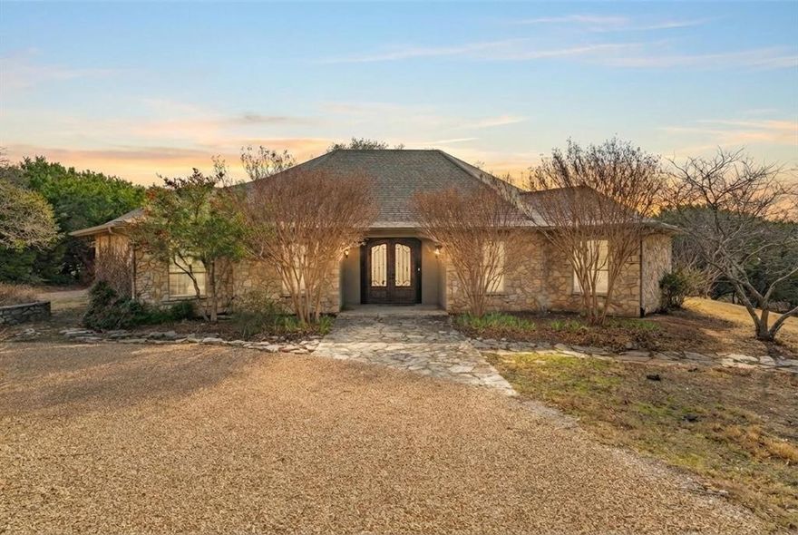 Don’t miss this exceptional Hill Country getaway situated on 2 scenic acres with a tranquil pond. This well-maintained home is designed for both comfort and entertaining, featuring an incredible outdoor living space and peaceful Texas countryside views. The expansive covered back patio offers the perfect setting for outdoor cooking, dining, and relaxing while enjoying the views. Inside, the living room showcases soaring ceilings with rustic wood beams, a gas-log fireplace, and custom built-in cabinetry. The spacious dining area captures the same picturesque views and includes a well-appointed wet bar—ideal for hosting family and friends. The kitchen provides abundant cabinet and counter space along with a built-in refrigerator, making meal preparation both functional and convenient. The home features two generously sized primary ensuite bedrooms, thoughtfully split for privacy, each with a walk-in closet and private bath. Two smaller flex rooms offer versatility for home offices, reading nooks, bunk rooms, or storage. An oversized two-car garage provides ample room for vehicles, equipment, and recreational toys. The long, private driveway leads to a beautifully landscaped circular drive, creating an impressive arrival and offering abundant guest parking. Water is supplied by a shared well with five neighboring properties at just $50 per month. Enjoy added privacy and minimal traffic with this cul-de-sac location on a dead-end road. Conveniently located in Glen Rose ISD and just minutes from Fossil Rim Wildlife Center and Dinosaur Valley State Park. Whether you’re seeking a weekend retreat, full-time residence, or family getaway, this Hill Country property delivers privacy, charm, and timeless Texas appeal.