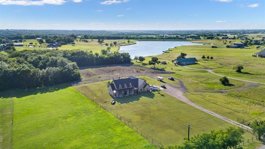 This stunning gated lakefront estate is situated on 3.6 acres in the highly desirable Rockwall ISD, offering a rare opportunity to own a one-of-a-kind ranch-style stone home with a fully equipped barndominium and horse facilities. Discover the perfect blend of luxury, privacy, and country living just minutes from downtown Rockwall and I-30. Step through custom wrought-iron double doors into an interior rich with charm and craftsmanship—featuring hand-scraped hardwood floors, travertine stone tile & a full masonry fireplace perfect for cozy winter nights. 
The open-concept floor plan is ideal for entertaining, showcasing a chef’s kitchen with commercial-grade stainless steel appliances, granite countertops, and ample prep space.
The luxurious primary suite boasts an oversized walk-in closet with direct access to the laundry room, a spa-inspired bathroom with a slate walk-in shower & a copper clawfoot tub. Two additional downstairs bedrooms share a stylish Jack-and-Jill bath with custom whiskey barrel sinks & large walk-in closets. Upstairs, you'll find a spacious second master suite or potential game room,media room with a private full bath & walk-in closet.
Enjoy plantation shutters, high-end finishes throughout and panoramic views of the private lake and surrounding pastures from the covered back patio. 
Also available is an exceptional 2000+ SF barndominium featuring: living quarters with private entry, large workshop area, three premium horse stalls with windows. Designed for comfort, privacy, and multi-use living. Perfect for equestrian lovers, hobbyists, or those seeking a peaceful retreat with luxury amenities and room to grow. MLS 21099578.