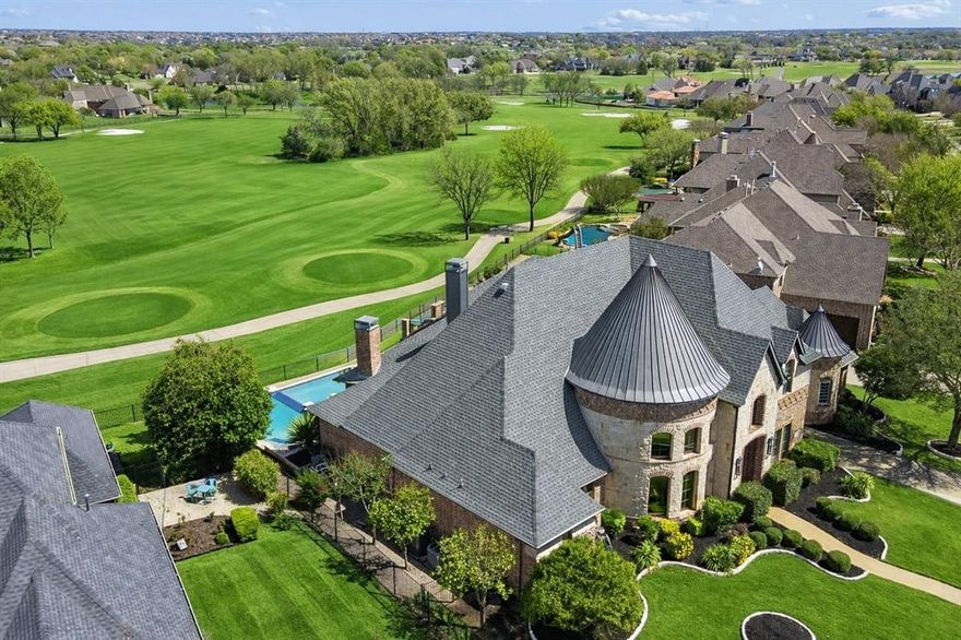Overlooking the 16th green and 17th tee boxes of Gentle Creek Golf Course, this remarkable 5-bedroom home offers a front row seat to one of Prosper’s most beautiful golf course settings. With uninterrupted fairway views and zoned to Walnut Grove High School in highly acclaimed Prosper ISD, the home combines striking architectural design with contemporary updates throughout. The entry immediately sets the tone. Marble floors with wood inlay lead to a dramatic curved staircase illuminated by a stunning crystal chandelier that creates an unforgettable arrival. A private study with soaring ceiling and custom built-ins provides an impressive workspace. The living room opens with impressive scale, while accordion glass doors span the back wall, opening to the covered patio and drawing the golf course scenery directly into the living space. The kitchen features marble countertops, a dramatic waterfall island, and top-tier appliances. The formal dining room connects through a butler’s area with a built-in desk, while a wine cellar tucked beneath the staircase provides a beautiful and unexpected showcase for collectors. The downstairs media room creates the perfect retreat for movie nights or watching the big game, complete with theater seating, surround sound, and a wet bar. Each bedroom in the home is ensuite, providing privacy and comfort for family and guests. The primary suite is positioned with golf course views and features a detailed tray ceiling and spa-inspired bath with oversized multi-head marble shower, freestanding soaking tub, and custom walk-in closet. Upstairs features a game room with balcony, dry bar, and two secondary suites. The golf cart garage was converted into a guest suite with stunning marble shower. Outdoors, a dual-tier pool and spa with waterfall features overlook the course, while the covered patio with fireplace, motorized screens, and outdoor kitchen creates a space designed for gatherings and unforgettable sunsets across the fairway.