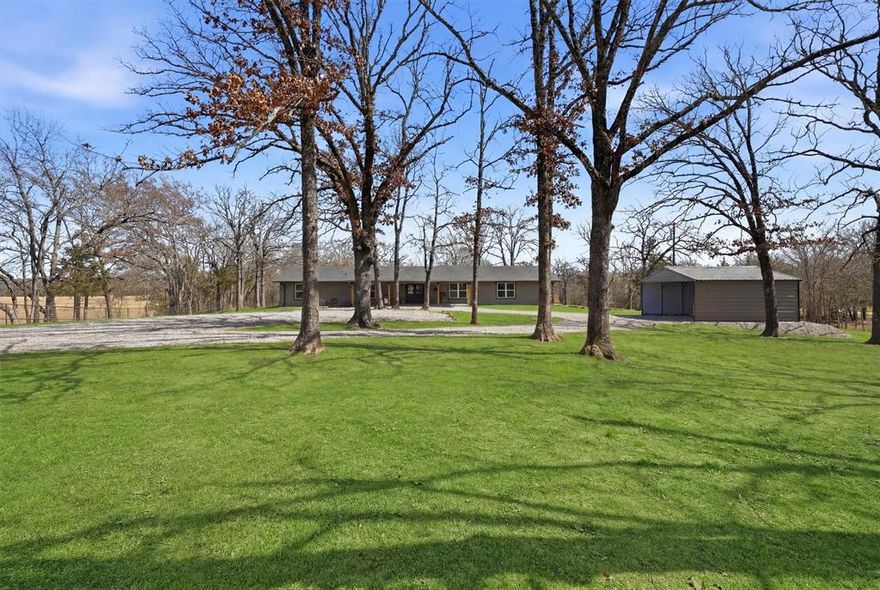 Welcome to 230 Frosty Hollow Rd in Denison, TX-an exquisitely renovated Modern Rustic nestled on almost three tranquil, wooded acres. This property seamlessly blends rugged allure with contemporary luxury, crafting a serene sanctuary enveloped by the natural world. Upon arrival, the expansive covered front and rear porches establish a sophisticated ambiance-perfect for savoring morning coffee, hosting elegant gatherings, or immersing in the serene vistas of the surrounding flora and fauna. Inside, the Modern Rustic , exudes a cozy elegance with its vaulted ceilings, exposed beams, and a striking stone fireplace showcasing a new pellet stove as the focal point of the spacious living space. The redesigned kitchen boasts bespoken cabinetry, elegant countertops, floating shelves, and state-of-the-art stainless steel appliances seamlessly merging style with functionality. The expansive utility room provides ample storage, a designated space for extra refrigeration, and practical built-in counters for organization. A bonus living area offers versatility as a game room, media lounge, or convenient guest retreat, adjacent to to the fifth bedroom and full bath. The primary suite promises an oasis of tranquility with its lavish ensuite bath, expansive walk-in closet, and additional storage area. Boasting 5 bedrooms in total, this residence offers ample space for all the freedom to establish a home office, fitness area, or creative studio tailored to your lifestyle. Venture outdoors to explore your private haven in nature-towering trees, verdant lawns, and meandering trails that lead to a serene creek bed. Whether unwinding on the porch or traversing the grounds, this property embodies the peaceful essence of rural-living mere moments from the heart of the city. New double carport plus several recent upgrades complete this exceptional offering. Minutes from downtown Denison-voted one of Texas' Best Downtowns for Shops and Restaurants.