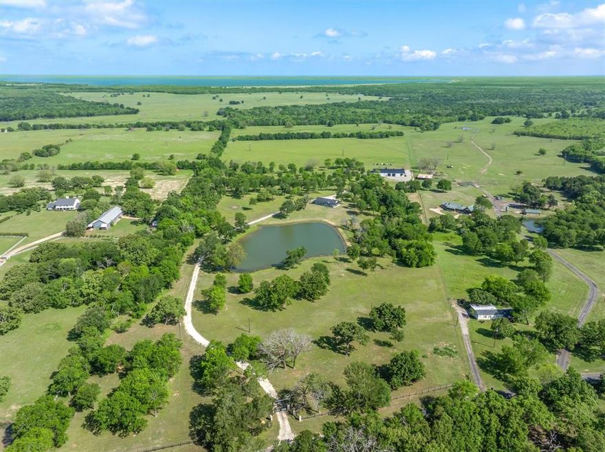 Within 1 hour of Dallas- World-class 408± acre hunting resort The T River Ranch with over 3,000 feet of Sabine River frontage, where historic McBee Creek winds through towering oak forest, & wildlife-rich hardwood bottoms. Fenced on both sides all the way to river & absolutely loaded with wildlife in all forms, this ranch features a spring-fed duck slough off the old river channel, plus strategically placed high-end deer stands & protein feeders that all convey. At the heart of the property is an impressive 12,000± SF barndominium with 3 large bedrooms, open-concept kitchen & living area, laundry room, gun room, & approx. 9,000± SF of closed cell foamed shop space complete with half basketball court, air compressor, & two car lifts, including a drive-on lift. Outside the shop is 2 elec wench & sink cleaning station. Offering two separate private primary suites with ensuite baths & walk-in tiled showers, while the chef’s kitchen showcases high-end Café appliances, porcelain farm sink, quartz countertops, & an oversized island; all furniture & 9500-series TVs in barndo can remain, creating a true turn-key retreat. Step outside to a covered patio overlooking rolling hay fields & majestic oaks, with fiber-optic internet & a cell booster ensuring modern connectivity in a private, end-of-the-road setting. The property is in ag for wildlife & hay.  Additional improvements include select camera systems & generators convey. Within walking distance is a 1,500± SF additional 2023 farmhouse style guest house with 2 private bedrooms, 2-bath & 2-car garage, vaulted ceilings, built-ins, quartz counters, soaking tub, & large L-shaped shower. Kitchen windows in guest home open outward to frame a stunning water view of a 2± acre, professionally stocked pond—reported at roughly $40,000 in fish, including bass, bluegill, hand-released trophy bass, and catfish—along with all appliances, two ATVs, 1 tractor to convey, making this an exceptional, ready-to-enjoy East Texas river ranch.