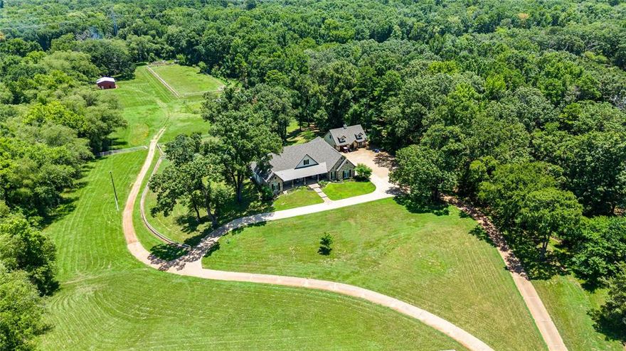 Discover serenity on 20.179 acres, just 7.5 miles from Tyler's medical district. This estate boasts a 4,152 Sq. Ft. main house, complemented by a guest house offering 1,620 Sq. Ft. Impeccable craftsmanship is showcased throughout, scraped wood flooring, Pella windows, and 8-foot solid 3 foot wide doors. The main house has a study with a library wall and built-in ladder, a formal dining room, and a family room with a stone fireplace opening to the expansive gourmet kitchen which is a culinary masterpiece, equipped with abundant cabinetry, a designer vent-a-hood, built-in refrigerator, KitchenAid appliances, double ovens, 2 islands, and bar seating for 10. Each bedroom in the main house boasts an ensuite bathroom. The second living area offers flexibility as a fourth bedroom. The guest house features 2 bedrooms, 2 baths, and a 1 car garage. Outside, a barn with horse stalls, a loafing shed, arena, and hay building. A 4 car garage and home generator ensure convenience and peace of mind.