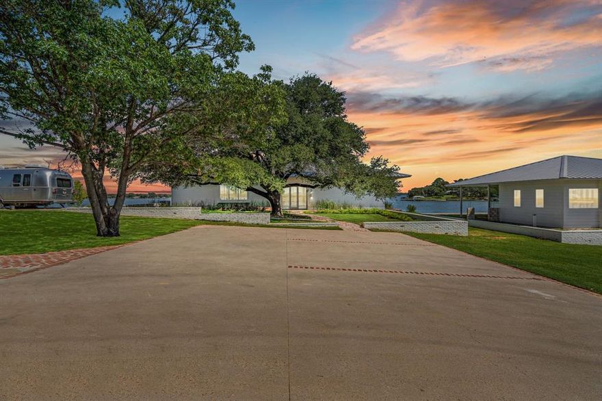 This single-story Eagle Mountain Lake retreat, designed for effortless lakeside entertaining, sits gracefully on 2.164 acres with 750 feet of waterfront. The open-concept layout is framed by floor-to-ceiling windows that showcase sweeping lake views, while a chef’s kitchen boasts a marble island, Miele appliances, and four refrigerator drawers, with a laundry room that doubles as a secondary walk-in pantry. A covered porch wraps around three sides of the home, complete with a built-in bar top and serving area, and beyond the patio a manicured turf yard provides a serene setting for relaxation. The floating dock with boat and jet ski lift enhances the lakefront lifestyle. Prepared for future expansion, the home includes a large attic as well as a separate 1,200-square-foot suite nearing completion, offering panoramic views, private his-and-hers ensuites, and separate closets. Additional amenities include a gated drive with RV and boat parking, plus an Airstream, boat, and jet skis—making this the ultimate turnkey lake property.