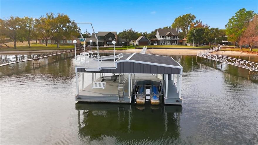 Sage Circle Beach House – Luxury Lakefront, Fully Renovated, and Exceptionally Rare Sandy Beach.  Your family is guaranteed to absolutely love this beautifully renovated two-story lakefront retreat tucked behind a private gated entry in one of the most sought-after locations on the Peninsula. Surrounded by impressive lake estates, this property delivers an unbeatable blend of privacy, luxury, and designer-finished comfort. The home opens to a dramatic two-story living room filled with natural light from an expansive lake-facing wall of windows. A soaring floor-to-ceiling stone fireplace creates a stunning centerpiece for lakeside living. Elegant dining areas flow easily from the main living room. The main-level primary suite provides quiet convenience, and its master closet doubles as a saferoom. Every bathroom has been recently redone with modern, upscale finishes that feel fresh and sophisticated. Upstairs, three welcoming bedrooms and a spacious family room with private balcony offer the perfect layout for friends and family. Even more space awaits in the detached guest house, which adds a large private bedroom, a bunkroom, and full bathroom—making it ideal for visitors or maximizing rental appeal. Outside is where this home truly shines. The oversized lakefront is immaculate, professionally landscaped, and thoroughly irrigated with a lake pump. A generous outdoor living area sits between the main house and guest house, covered yard-side patio and upper-level observation balconies are for soaking in the views. The huge, lush lakeside lawn leads to a naturally occurring sandy beach perfect for children. A grandfathered long walkway reaches out to deep water beneath an excellent two-story dock in near-perfect condition. With its prime setting, extensive guest accommodations, stylish renovation, and unbeatable beachfront location, this Beach House offers outstanding potential as a complete turnkey short-term rental—or an exceptional personal getaway.