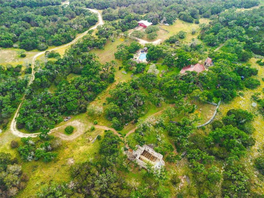 This stunning 20-acre Hill Country retreat is just 5 minutes from Wimberley and 10 minutes from San Marcos, offering the perfect balance of seclusion and accessibility with Austin and San Antonio nearby. The hand-built, 2,300 sqft log cabin offers total privacy and features vaulted ceilings, rustic cowboy and Native American-inspired decor, and a gourmet kitchen with mosaic tile backsplash, light granite countertops, custom cabinets, gas range, and stainless steel sink. Enjoy three fireplaces—two stone fireplaces in the dining and living rooms, and a wood-burning stove in the primary bedroom. The primary bath has a sculptural walk-in shower, while the second bath features a soaking tub with mesmerizing mosaic tiles. The expansive veranda leads to a koi pond, stone patio, and an elysian cabana. The property also boasts a hand-built stone chapel, ideal for weddings, concerts, and other events, seating up to 80 guests. Its rustic charm and timeless beauty transport you to another era, reminiscent of the spirit of Austin's past. Outdoor living includes a stand-alone pool, an outdoor kitchen with stone grill and fire pit, and a raised outdoor stage for performances, evoking the spirit of cosmic cowboys like Willie Nelson and Waylon Jennings. Horse amenities include a barn with stables and corral, and a grand stone rabbit house. The property offers easy access to Ranch Road 12 and is close to downtown Wimberley, Hill Country Studios, Jacobs Well, and other attractions. It has served as both a short-term rental and a cherished homestead. This unique Hill Country gem combines luxury, rustic charm, and artistic beauty, offering endless possibilities—whether for a private retreat, income-generating rental, or event venue. Don't miss out on this rare opportunity!